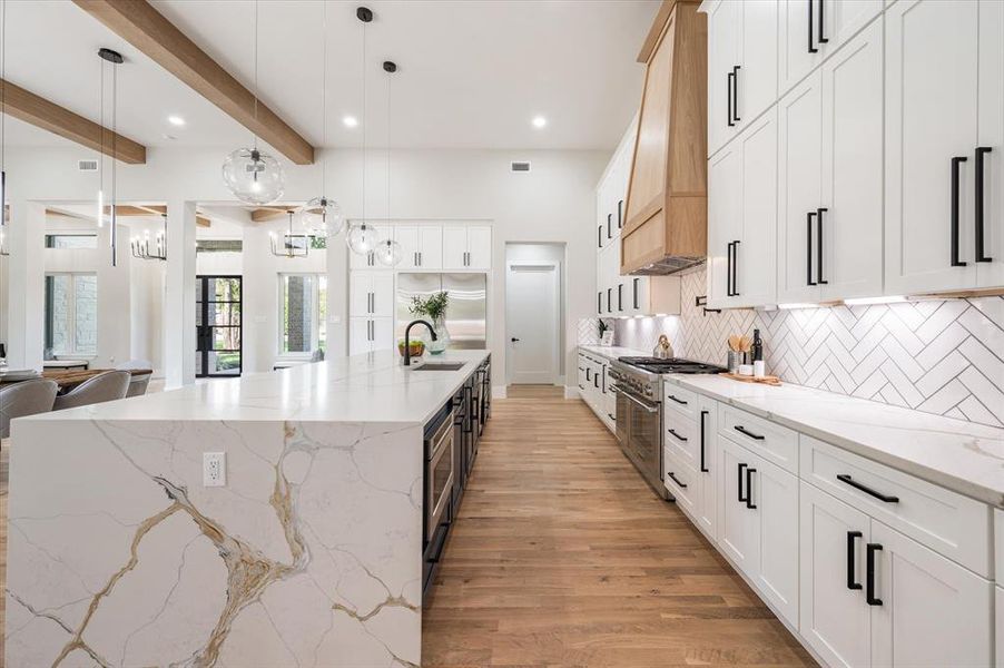 Kitchen featuring light stone countertops, pendant lighting, light hardwood / wood-style floors, sink, and a large island with sink