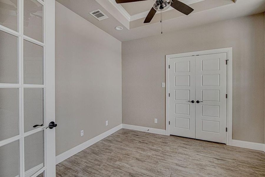 Spare room with a raised ceiling, light wood-type flooring, and ceiling fan