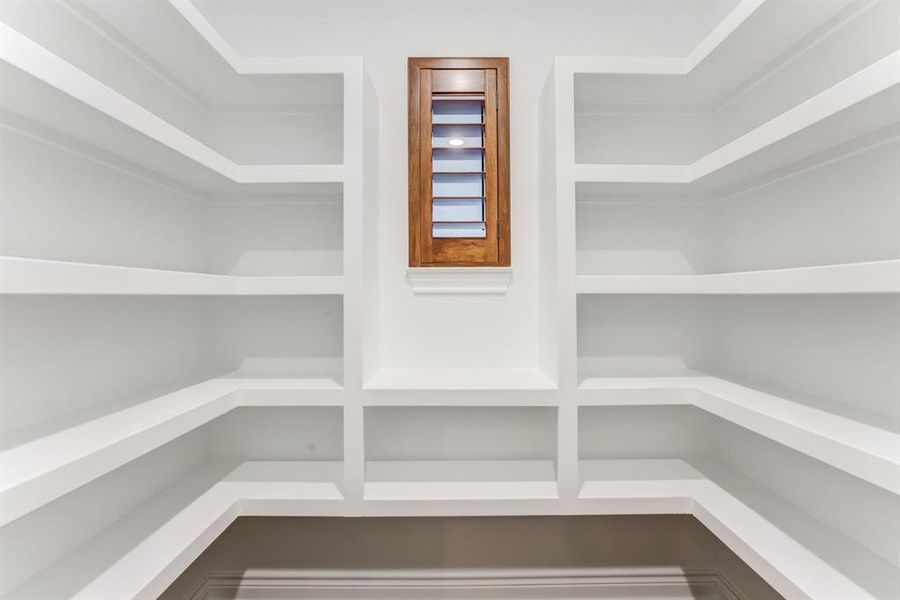 Extensive white shelving and a small window allowing for natural light offers space for organizing bulk items and small appliances in the pantry.