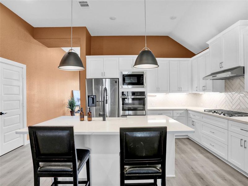 Gorgeous modern kitchen with double ovens, quartz counters, farmhouse sink, island and gas stovetop.