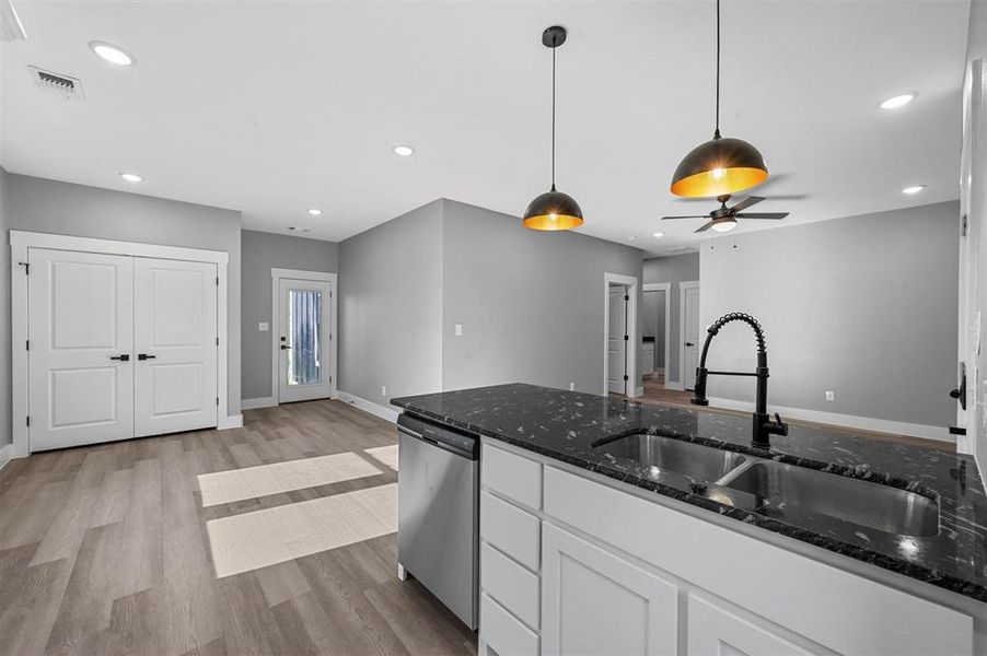 Kitchen featuring ceiling fan, hanging light fixtures, white cabinetry, dishwasher, and dark stone countertops