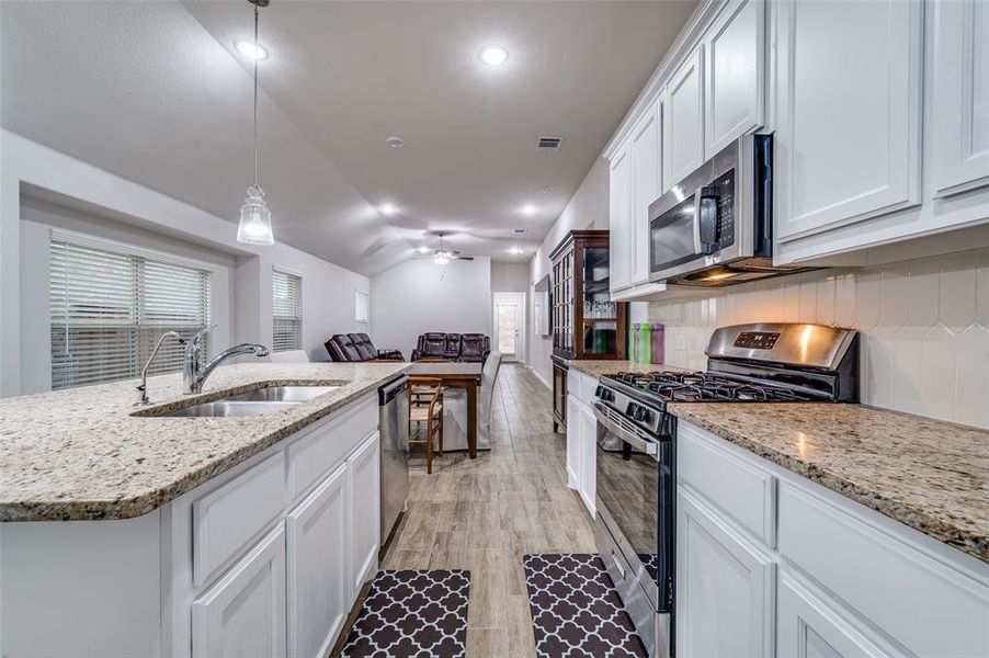 Kitchen with sink, hanging light fixtures, stainless steel appliances, a kitchen island with sink, and white cabinets