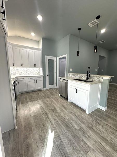 Kitchen with hanging light fixtures, appliances with stainless steel finishes, white cabinetry, light hardwood / wood-style flooring, and sink