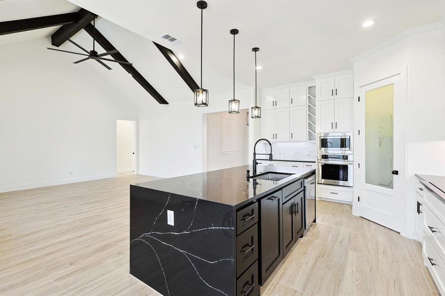 Kitchen featuring a kitchen island with sink, sink, stainless steel appliances, vaulted ceiling with beams, and ceiling fan