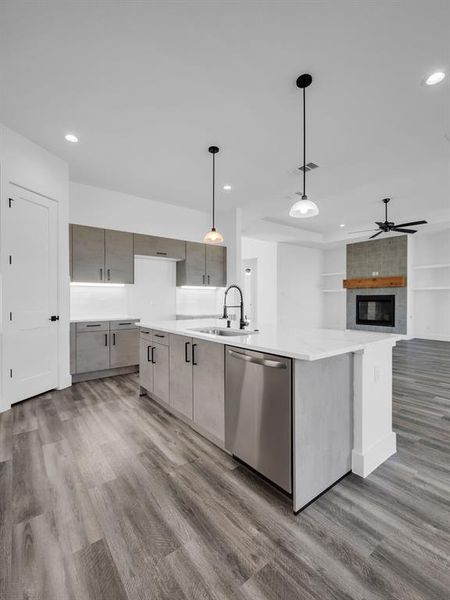 Kitchen with wood-type flooring, sink, a tiled fireplace, pendant lighting, and stainless steel dishwasher