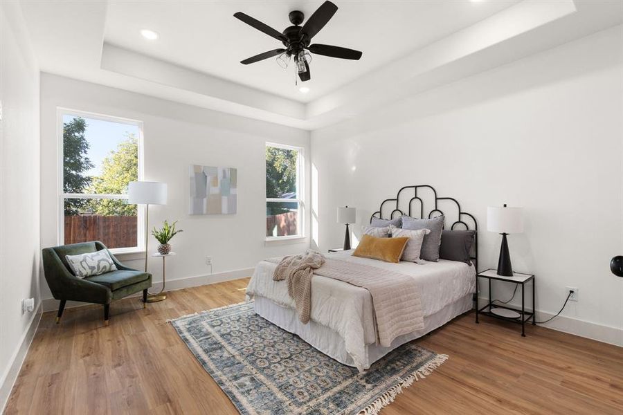 Bedroom featuring multiple windows, a tray ceiling, hardwood / wood-style floors, and ceiling fan