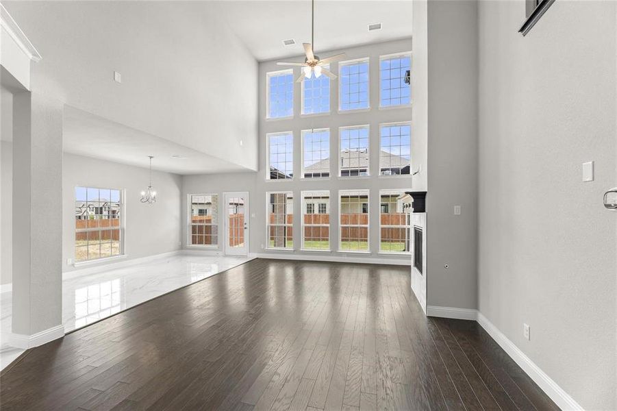 Unfurnished living room with ceiling fan with notable chandelier, a towering ceiling, and dark hardwood / wood-style flooring