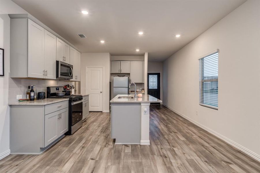 Kitchen featuring light stone countertops, stainless steel appliances, light wood-type flooring, and a kitchen island with sink