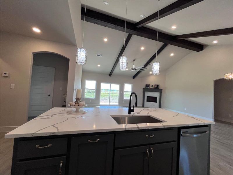 Kitchen with vaulted ceiling with beams, sink, a center island with sink, dishwasher, and light stone countertops