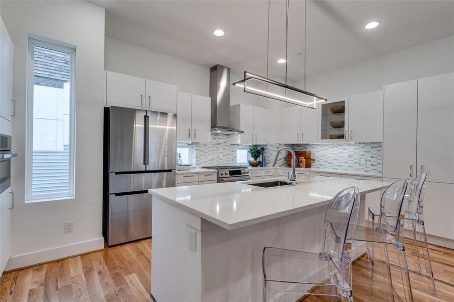 Kitchen with a kitchen island with sink, sink, white cabinetry, wall chimney range hood, and stainless steel appliances