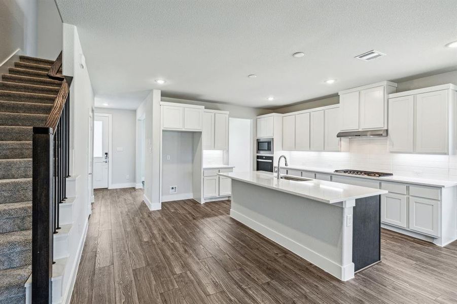 Kitchen with white cabinetry, stainless steel appliances, hardwood / wood-style flooring, and a kitchen island with sink