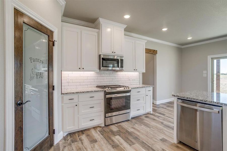 Kitchen with white cabinetry, light granite countertops, stainless steel appliances, and light ceramic tile wood-type flooring