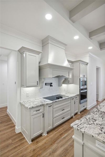 Kitchen with stainless steel appliances, wood-type flooring, backsplash, and custom exhaust hood