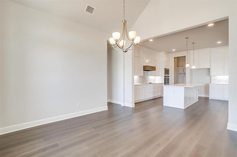 Unfurnished living room featuring a notable chandelier, sink, high vaulted ceiling, and hardwood / wood-style floors