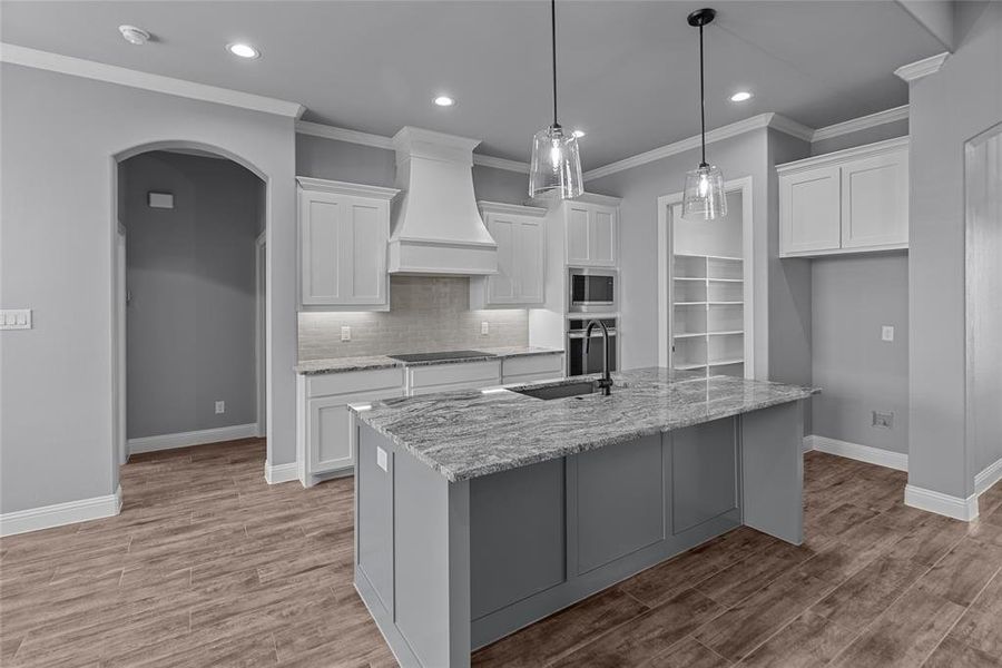Kitchen with custom exhaust hood, stainless steel appliances, light wood-type flooring, sink, and a center island with sink