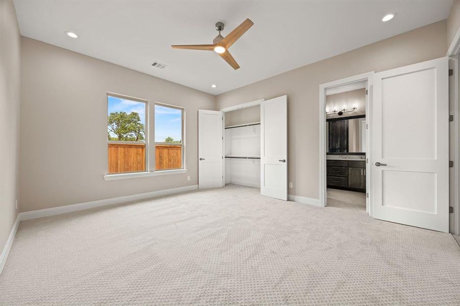 Unfurnished bedroom featuring light colored carpet, ensuite bath, and ceiling fan