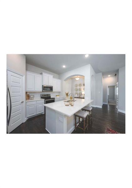 Kitchen featuring a breakfast bar, stainless steel appliances, dark wood-type flooring, a center island with sink, and white cabinets