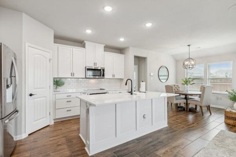 Kitchen featuring white cabinetry, stainless steel appliances, hanging light fixtures, a center island with sink, and backsplash