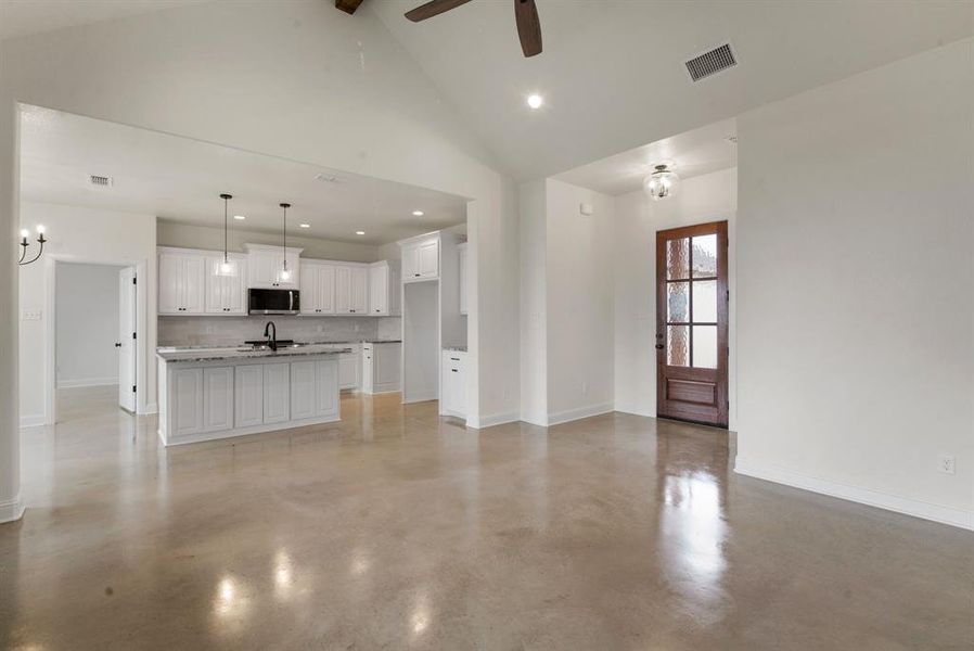 Unfurnished living room with ceiling fan with notable chandelier, sink, and high vaulted ceiling