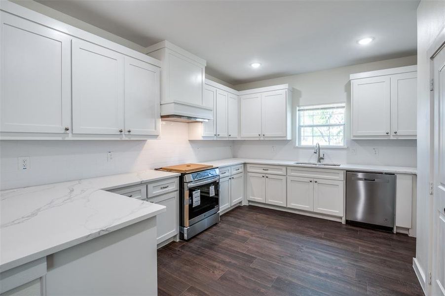 Kitchen featuring stainless steel appliances, sink, light stone countertops, white cabinets, and dark hardwood / wood-style flooring