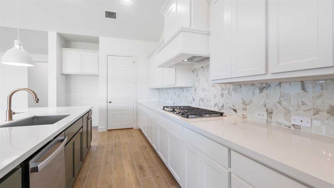 Kitchen featuring sink, hanging light fixtures, stainless steel appliances, white cabinets, and light hardwood / wood-style flooring