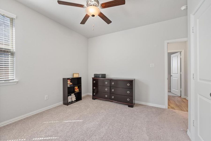 Carpeted bedroom with ceiling fan and natural light