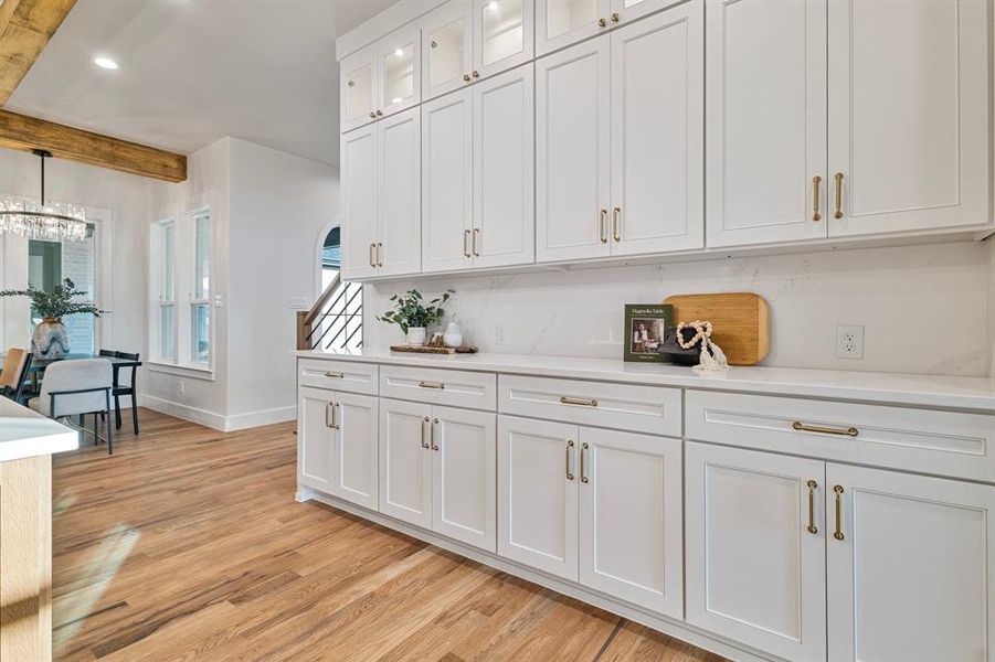 Kitchen featuring light hardwood / wood-style flooring, a notable chandelier, white cabinetry, beamed ceiling, and pendant lighting