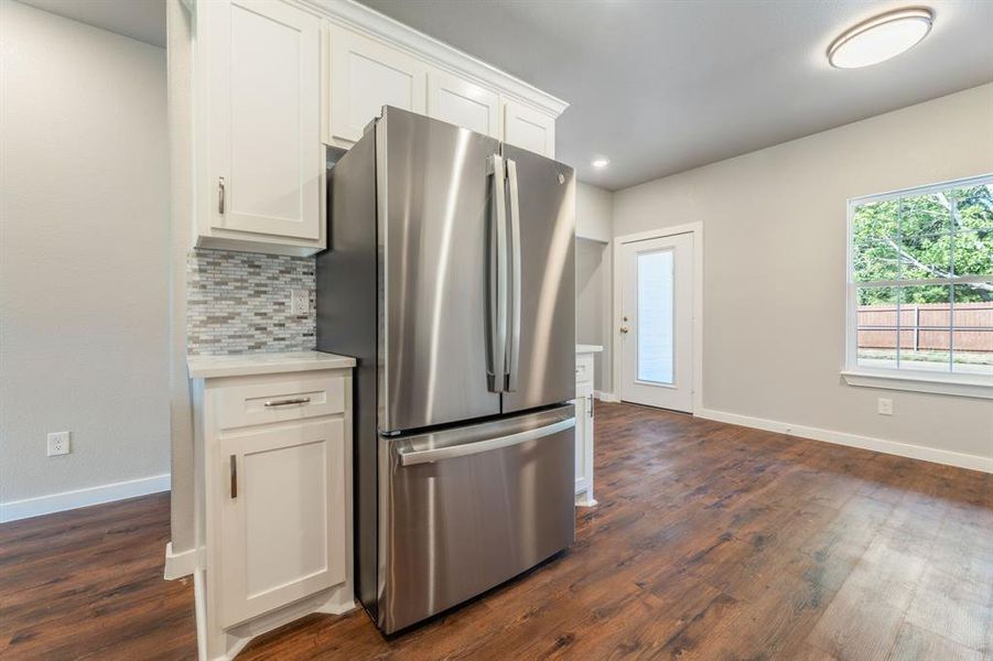 Kitchen with dark wood-type flooring, stainless steel fridge, white cabinets, and tasteful backsplash