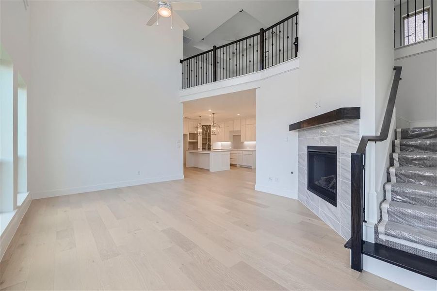 Living room with high vaulted ceiling, light hardwood / wood-style flooring, ceiling fan with notable chandelier, and a fireplace