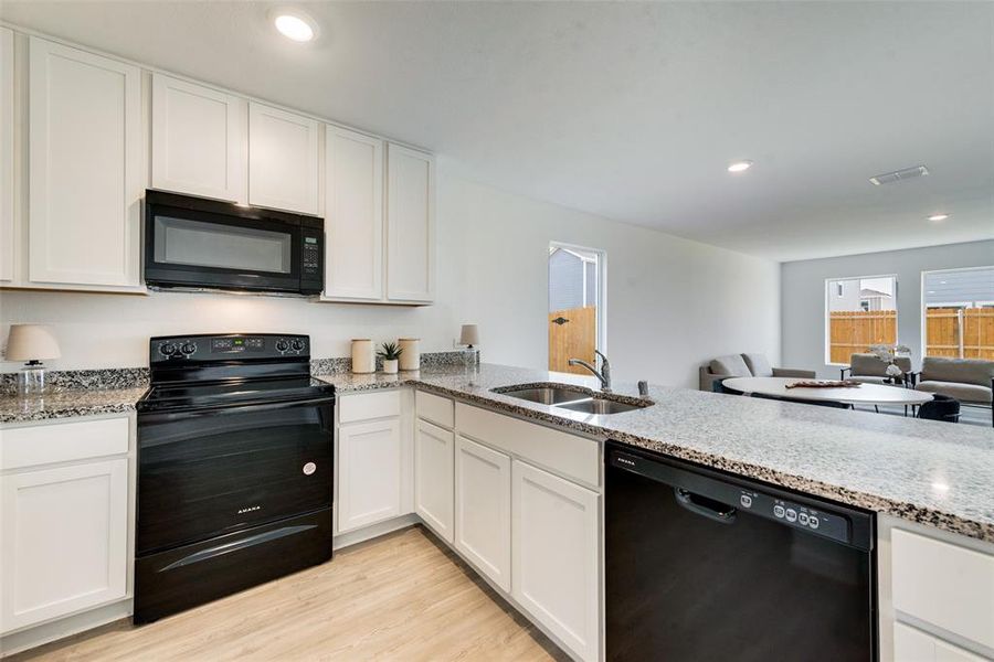 Kitchen with light wood-type flooring, kitchen peninsula, white cabinetry, black appliances, and light stone countertops