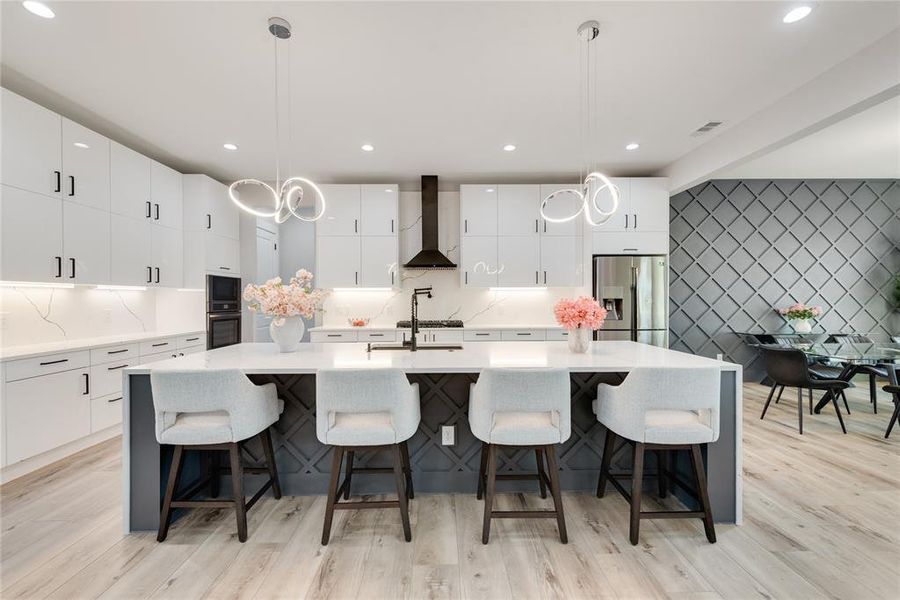 Kitchen featuring white cabinetry, appliances with stainless steel finishes, hanging light fixtures, and wall chimney range hood