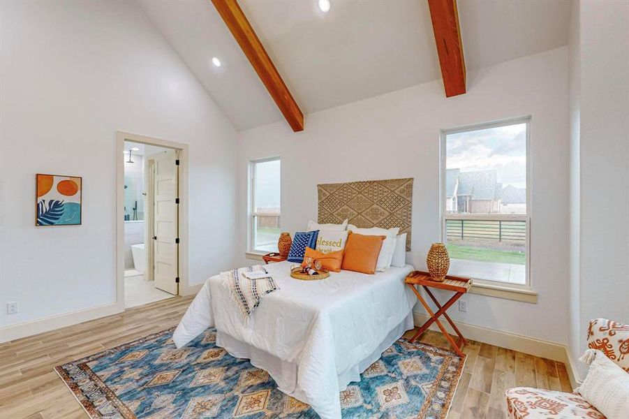 Bedroom featuring ensuite bath, light wood-type flooring, and vaulted ceiling with beams