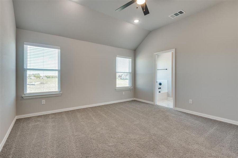 Carpeted primary room with a wealth of natural light, lofted ceiling, and ceiling fan