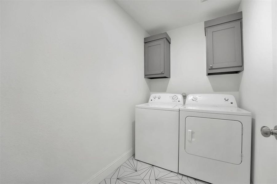 Clothes washing area with cabinets, washer and dryer, and light tile patterned flooring