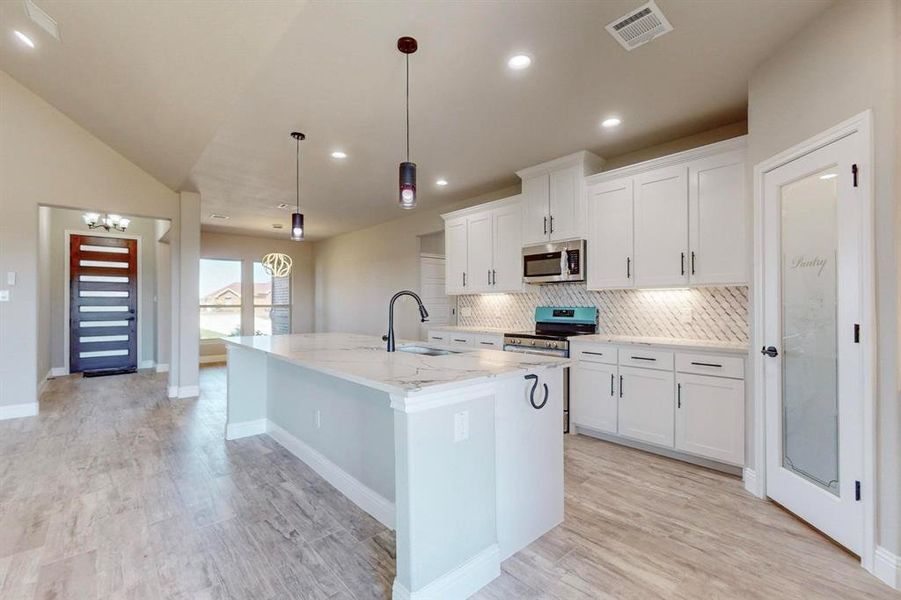 Kitchen with pendant lighting, sink, white cabinetry, stainless steel appliances, and a center island with sink