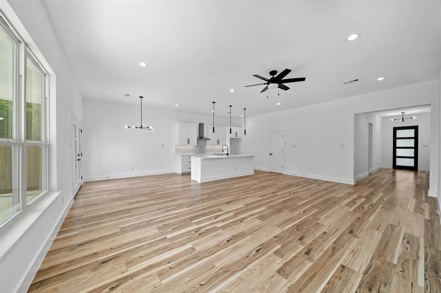 Unfurnished living room with sink, light hardwood / wood-style flooring, a wealth of natural light, and ceiling fan with notable chandelier