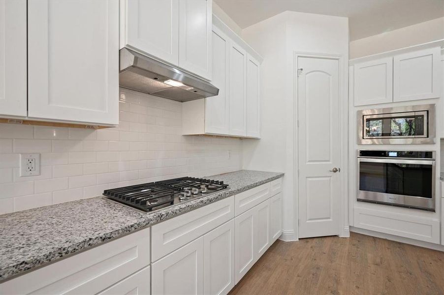 Kitchen with white cabinets, exhaust hood, appliances with stainless steel finishes, light hardwood / wood-style floors, and light stone counters