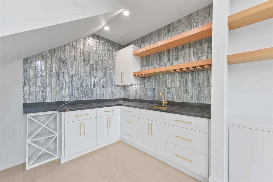 The wet bar highlights the designer finishes in this truly exceptional home. Open shelves combine with custom cabinets for ample storage. The attention to detail can be seen in the luxurious quartzite counter-tops, elegant tile backsplash and brass fixtures.