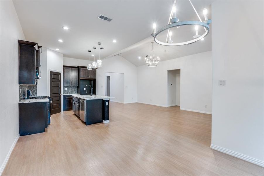 Kitchen with light hardwood / wood-style flooring, decorative light fixtures, sink, lofted ceiling, and an island with sink