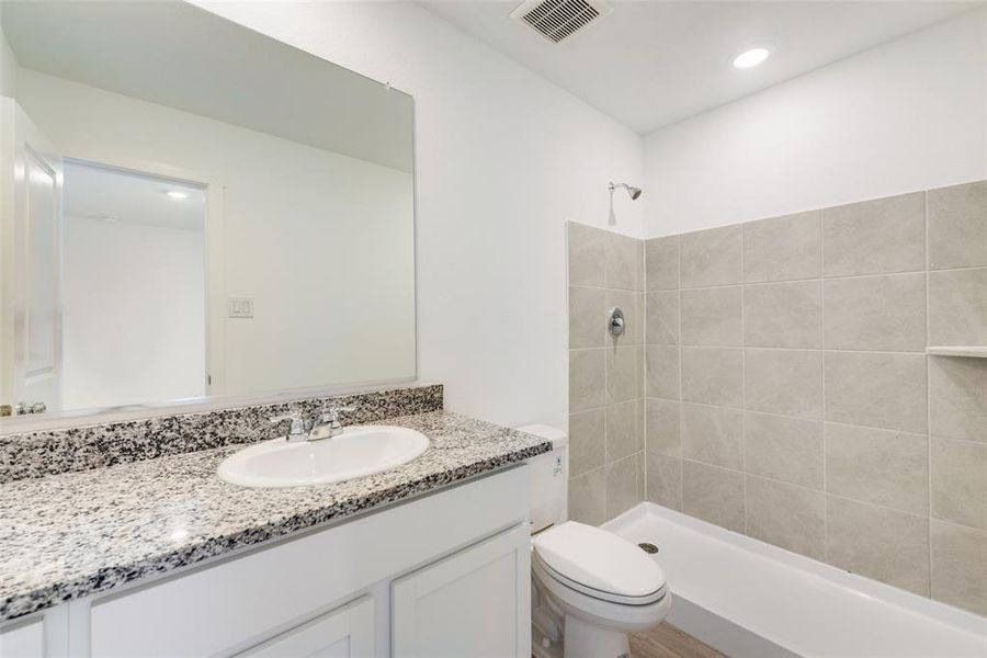 Bathroom featuring vanity, tiled shower, and toilet