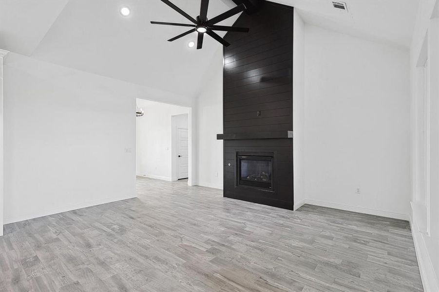 Unfurnished living room featuring high vaulted ceiling, ceiling fan, a fireplace, and light hardwood / wood-style floors