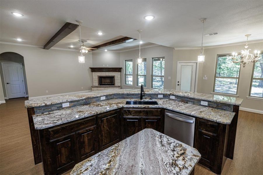 Kitchen featuring a large island with sink, light stone countertops, dark hardwood / wood-style flooring, stainless steel dishwasher, and sink