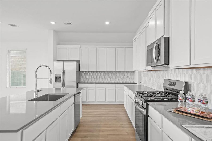 Open floor plan kitchen with quartz Countertop with oversize Breakfast island with all stainless-steel appliances, features white cabinetry,  stylish backsplash, complemented by recessed lighting and wood floors.