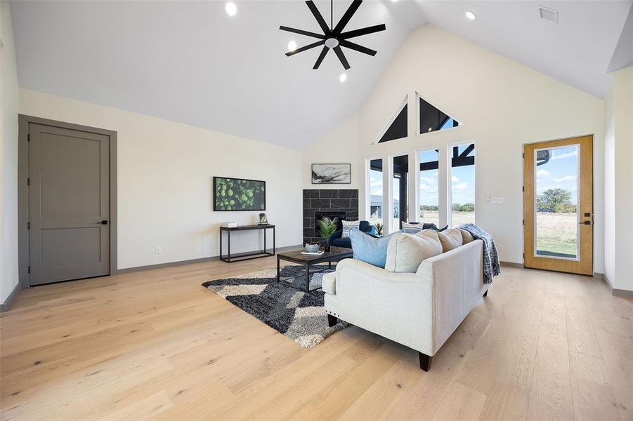 Living room with a tiled fireplace, high vaulted ceiling, light wood-type flooring, and ceiling fan