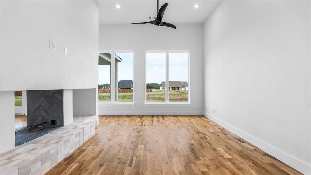 Unfurnished living room featuring ceiling fan, a tiled fireplace, and light hardwood / wood-style floors