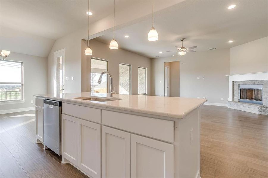 Kitchen featuring white cabinetry, a stone fireplace, ceiling fan, stainless steel dishwasher, and sink