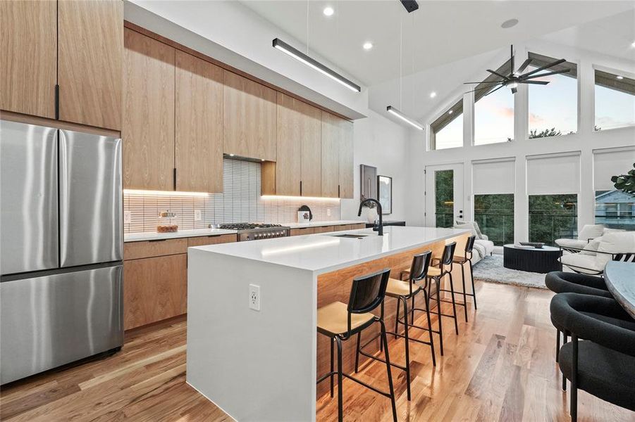 Kitchen with a center island with sink, stainless steel refrigerator, high vaulted ceiling, decorative backsplash, and ceiling fan