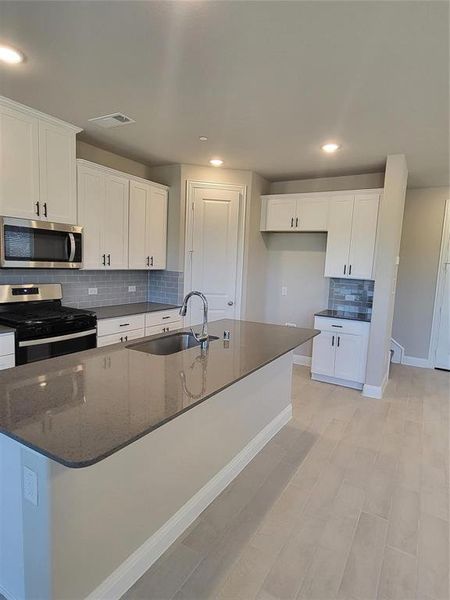 Kitchen featuring tasteful backsplash, gas stove, white cabinetry, and sink