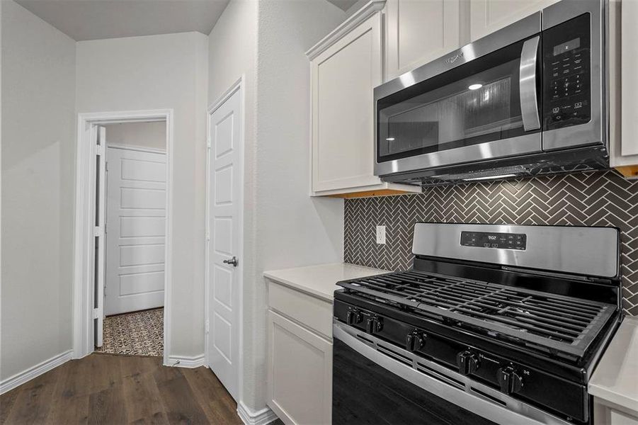 Kitchen with appliances with stainless steel finishes, white cabinetry, tasteful backsplash, and dark hardwood / wood-style floors