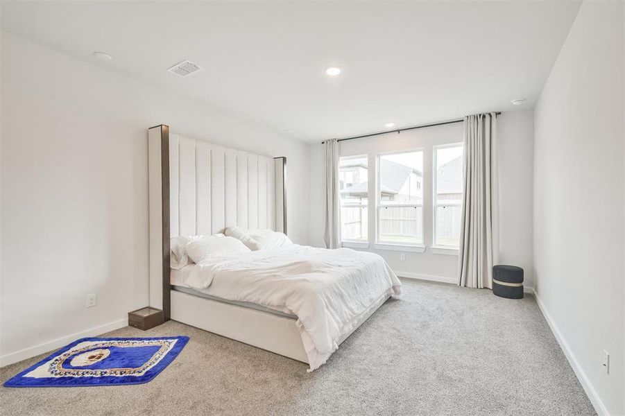 This is a spacious, well-lit bedroom with a large window, neutral color palette, and plush carpeting.